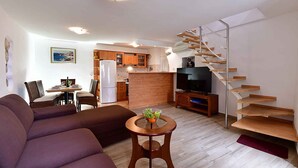 A modern living room with a sofa, a dining table with chairs, a kitchen area, and a spiral staircase. - Holiday home near the sea (Baška)