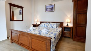 A neatly made bed with a floral bedspread, two bedside lamps, a wooden nightstand, a mirror, and a framed picture on the wall. - Holiday home near the sea (Baška)