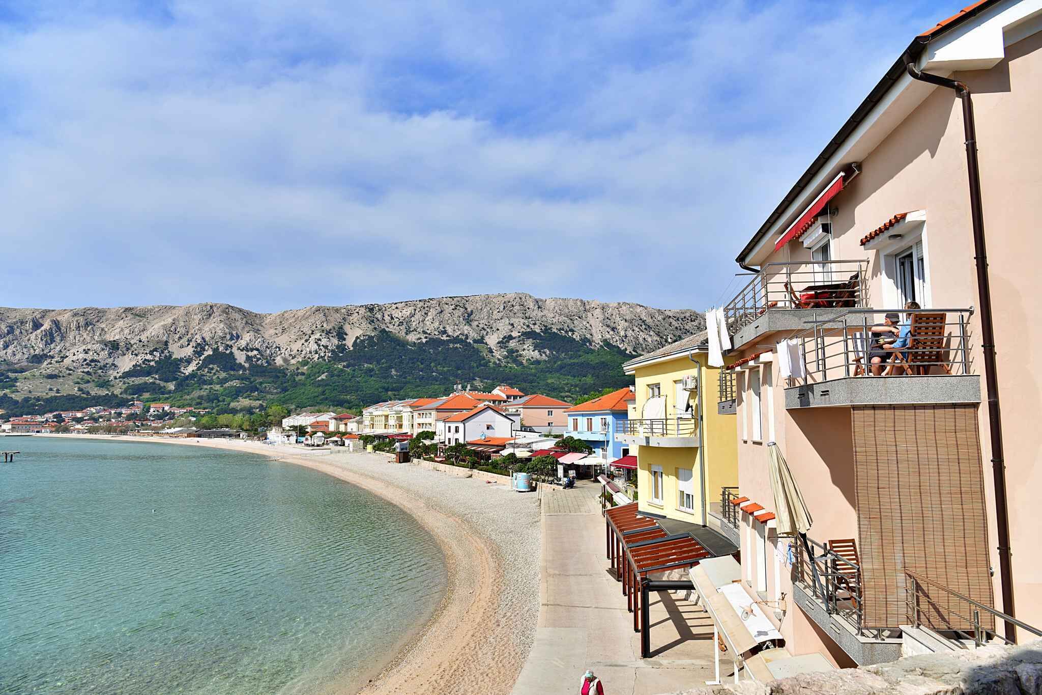 A coastal building with balconies overlooking a beach and mountains.