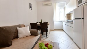 Un espace de vie compact comprenant un canapé, une table à manger et un coin cuisine équipé d’un réfrigérateur et d’un four à micro-ondes.