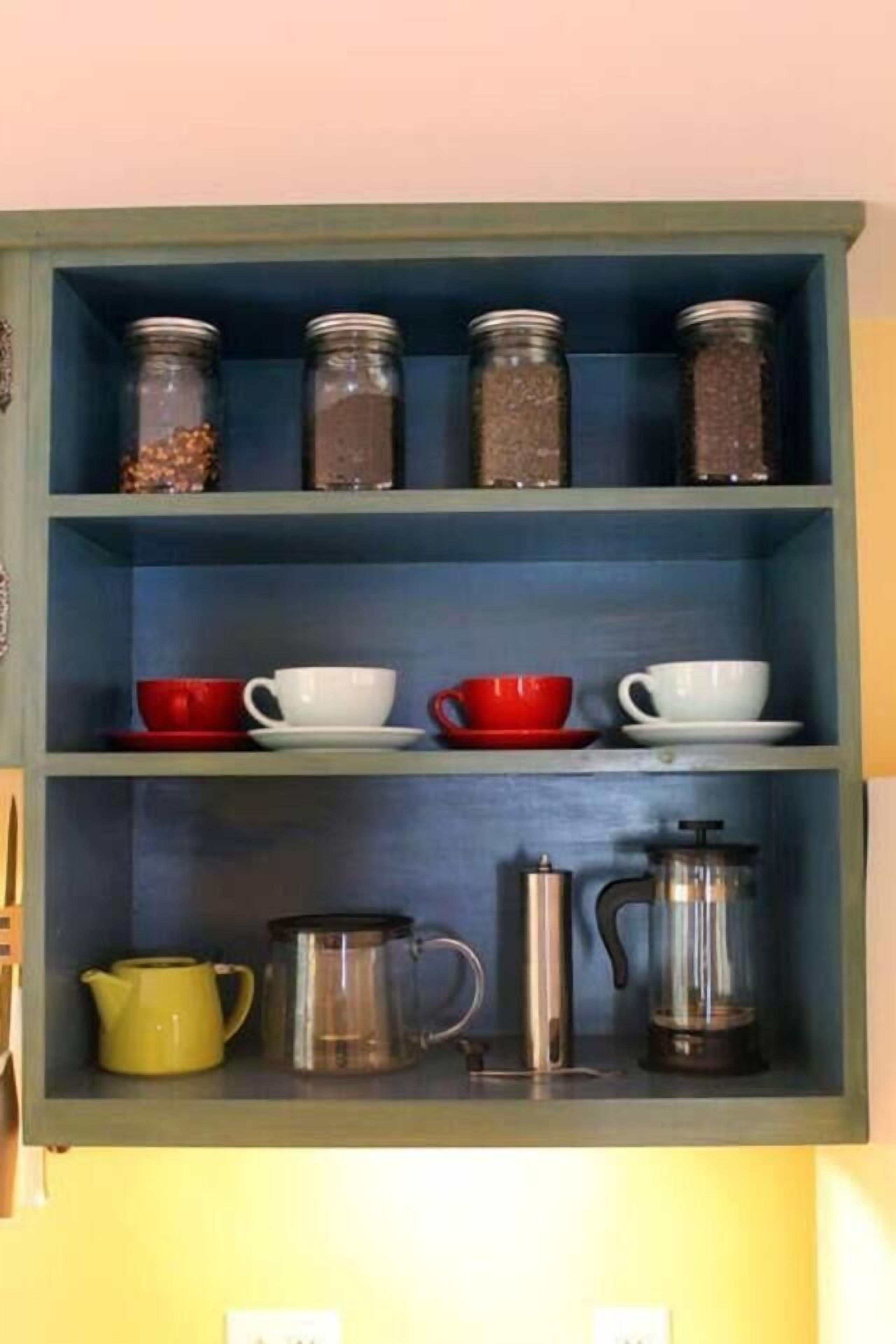 A kitchen shelf with jars, cups, and coffee equipment.
