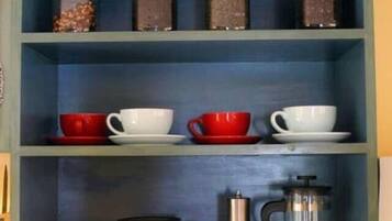 A kitchen shelf with jars, cups, and coffee equipment.