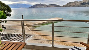 A balcony with a view of a lake, a wooden bench, and a striped lounge chair. - Holiday apartment with balcony and sea view (Baška)
