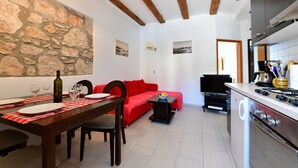 Une cuisine moderne dotée d’un four et d’une cuisinière encastrés, un coin repas avec une table et des chaises en bois, un canapé rouge et un mur en pierre.