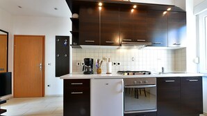 Une cuisine moderne avec des meubles de couleur sombre, un réfrigérateur blanc, une cuisinière et une machine à café.