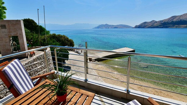 Un balcon donnant sur la mer, une chaise, un pot de fleurs et un mur en pierre.