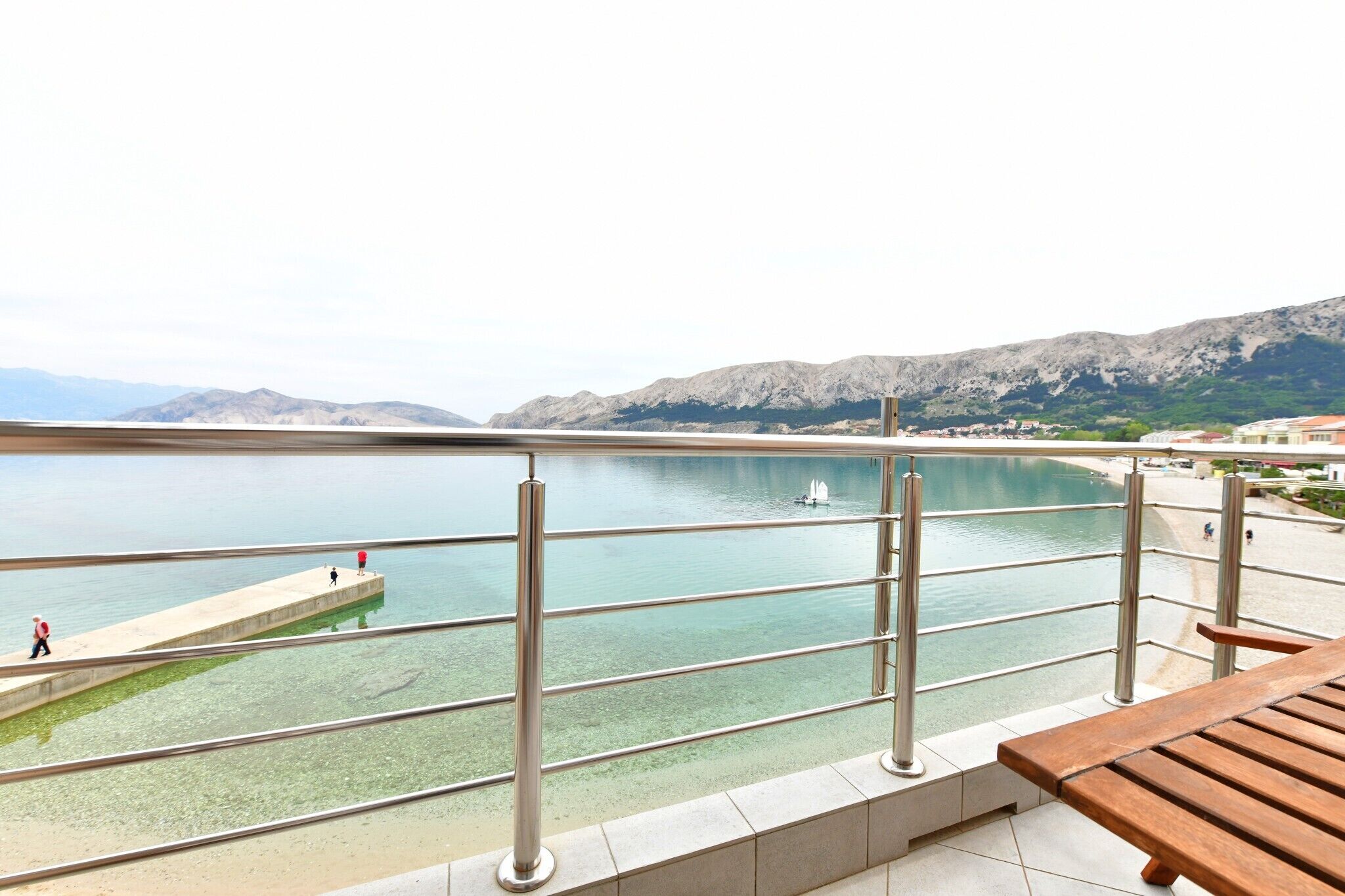Un balcon offrant une vue sur une étendue d’eau paisible, une plage de sable et des montagnes lointaines.