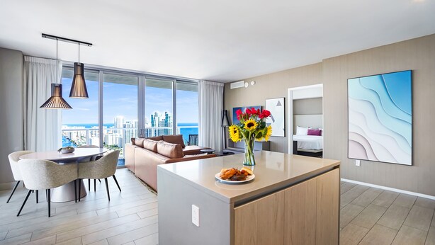 Een moderne woonkamer met een eethoek, een groot raam met uitzicht op de stad, een bank en een bijzettafeltje.