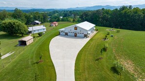 A large white building with a driveway leading to it, surrounded by green fields and trees.