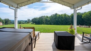 An outdoor patio with a covered seating area, a barbecue grill, and a view of a green field and trees.