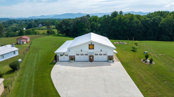 A large white barn with a sloped roof, surrounded by lush green fields and a mountainous backdrop. - The Sunflower Barn (Alexander)