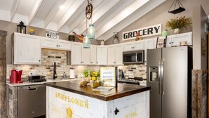 A kitchen with white cabinets, a stainless steel refrigerator, a wooden island, and a 'GROCERY' sign on the wall.