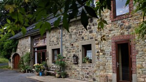 A stone building with a wooden door, a window with a flower box, and a bench outside. - La Grange- Historic flair and modern comfort in the midst of nature (Sourbrodt, Waimes (Belgien))