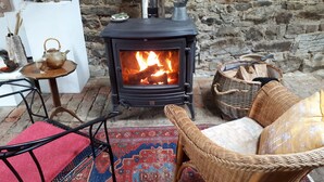 A cozy room with a wood-burning stove, wicker furniture, and a patterned rug. - La Grange- Historic flair and modern comfort in the midst of nature (Sourbrodt, Waimes (Belgien))