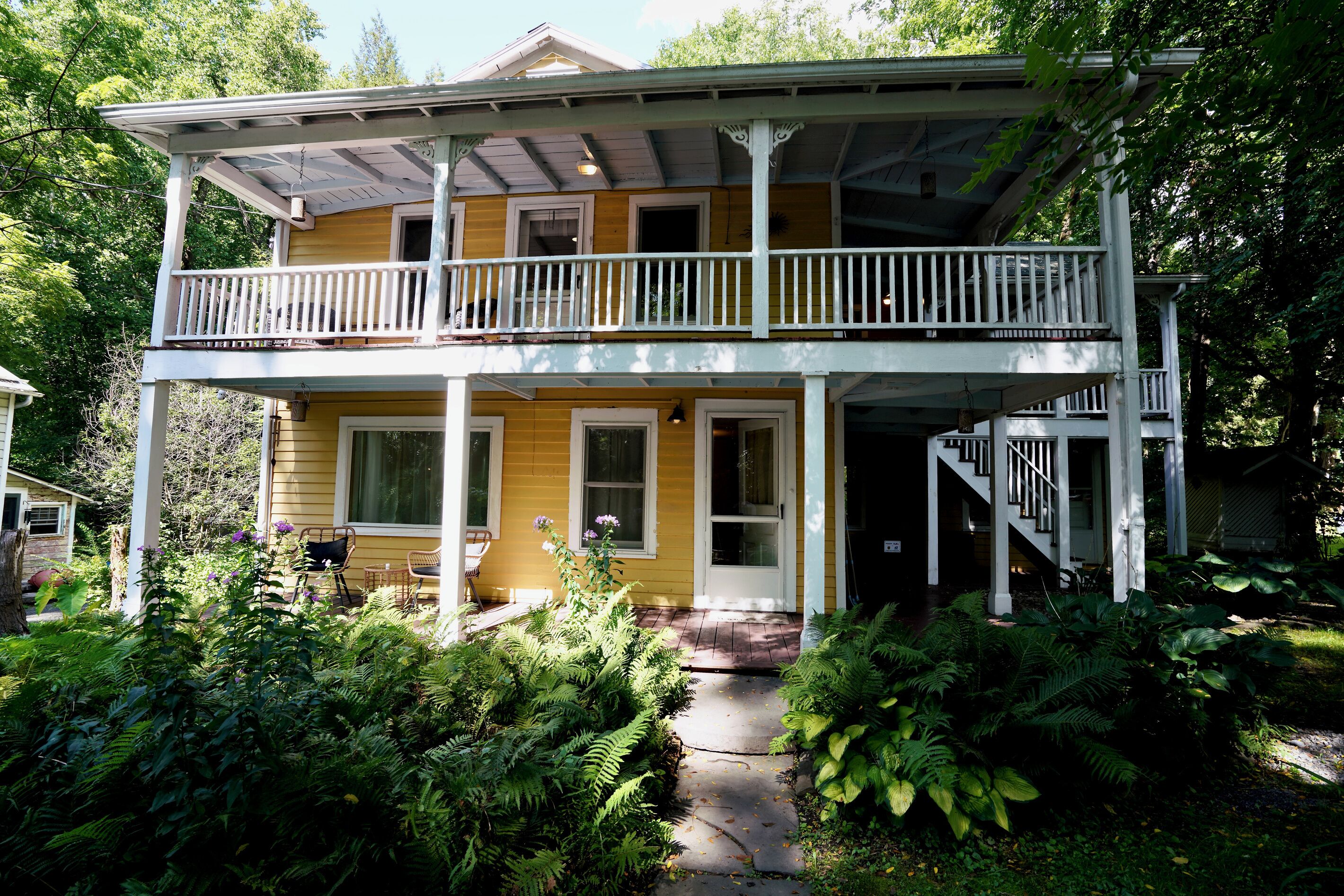 A two-story house with a balcony, a front porch, and a pathway leading to the entrance.
