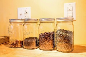 Cuatro frascos de vidrio con distintos contenidos sobre una superficie de madera, con un enchufe eléctrico al fondo.