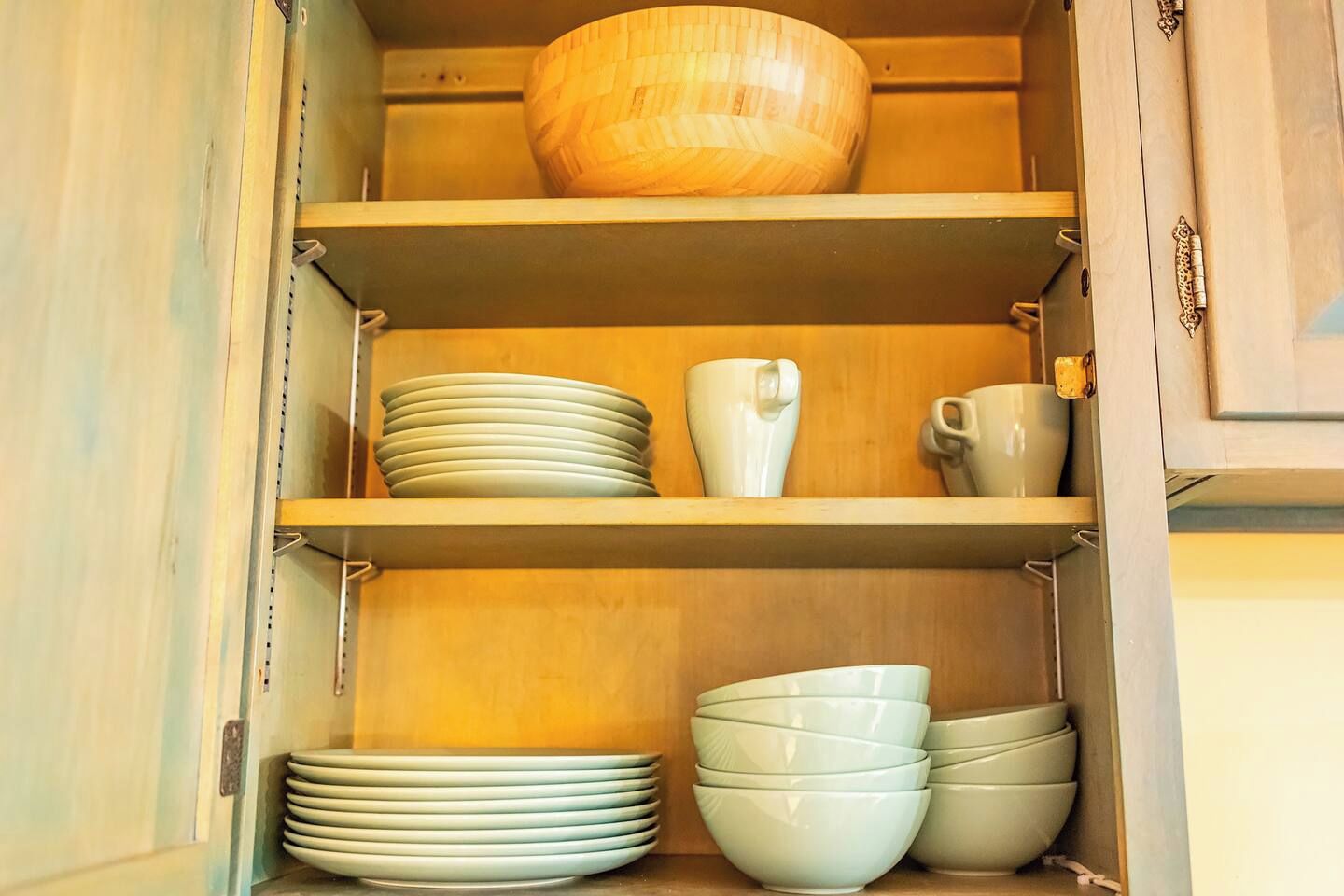 Un meuble de cuisine avec des étagères où sont rangées des assiettes, des bols et un saladier en bois.