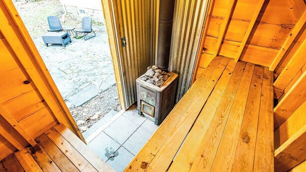 A wooden deck with a wood-burning stove and a door leading to an outdoor area with chairs. - Historic Hudson Valley Farmhouse w/ Sauna in Stone Ridge Hamlet (Stone Ridge)