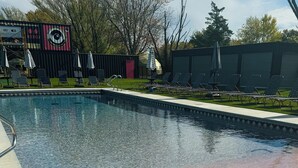 A swimming pool with lounge chairs and umbrellas, surrounded by trees and a building with a circular window. - Dome 3: Modern Boho Hideaway (South Haven)