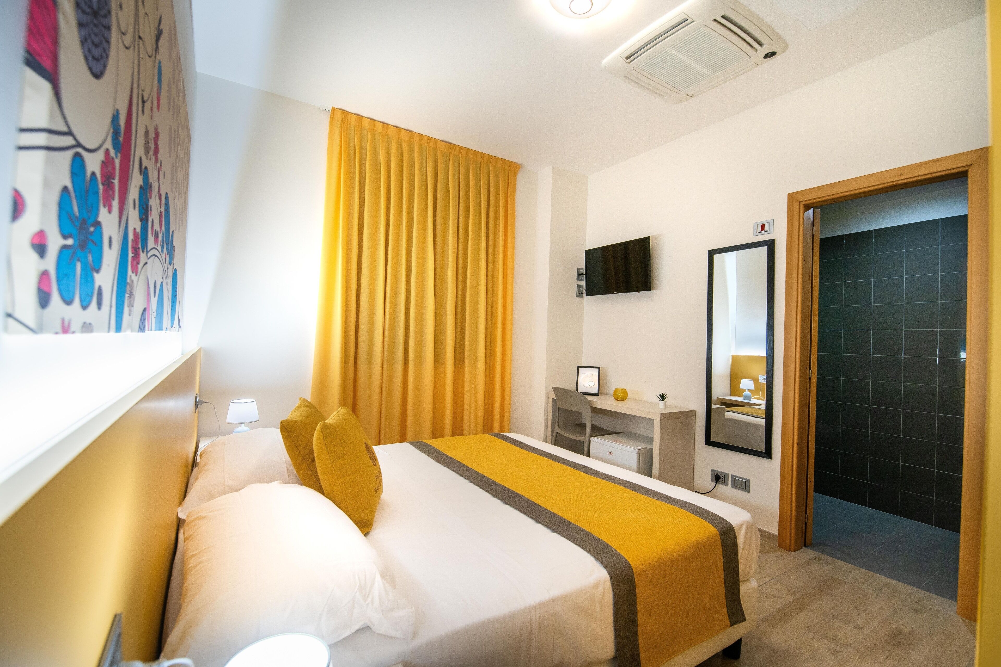 A hotel room with a bed, a desk, a chair, a television, and a bathroom with a shower.