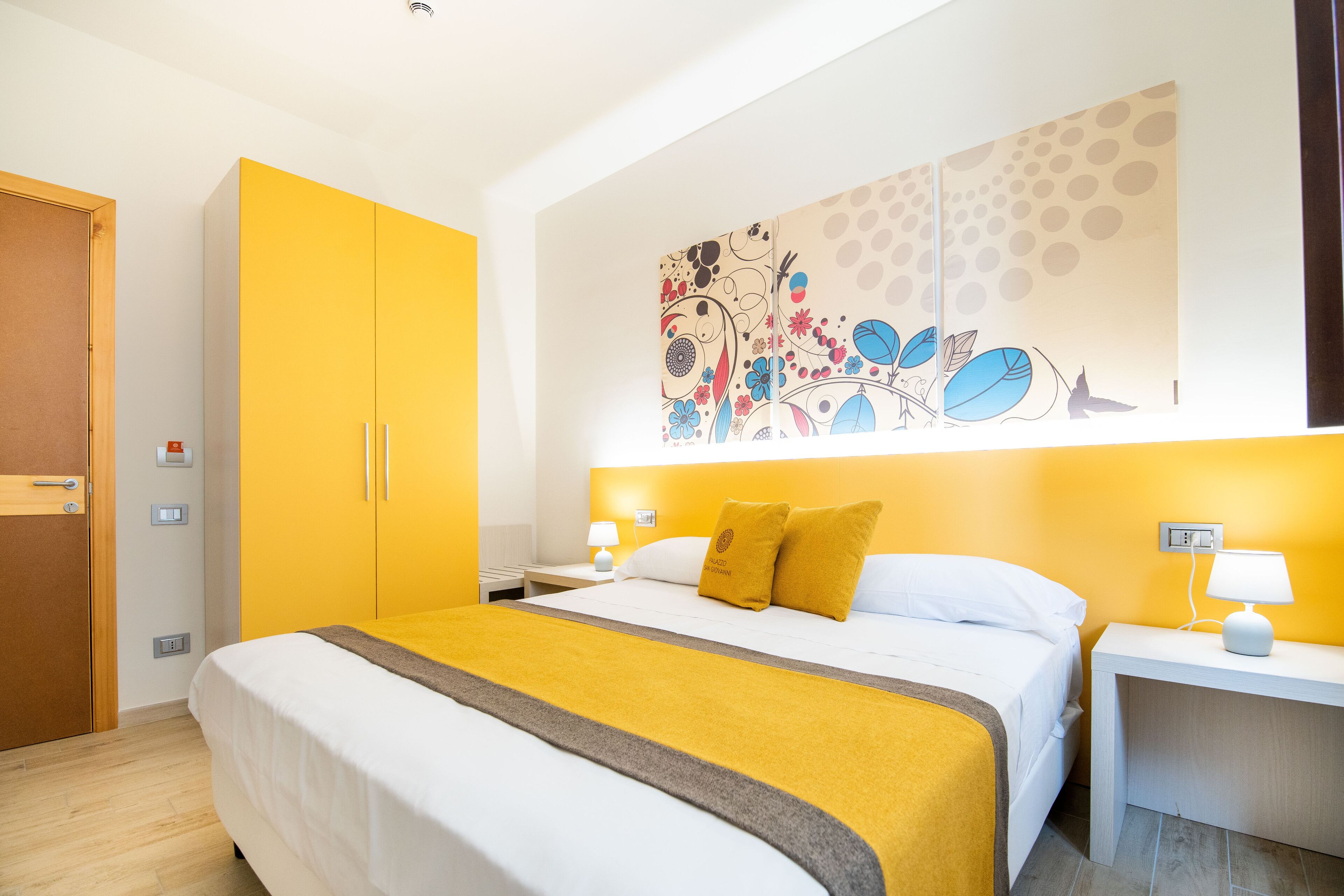 Une chambre d’hôtel comprenant un lit, une table de chevet, une armoire et une œuvre d’art murale.