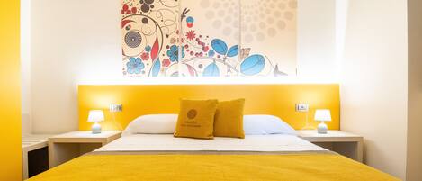 Una habitación de hotel con una cama, dos mesitas de noche, una obra de arte en la pared y una pared decorada en amarillo.