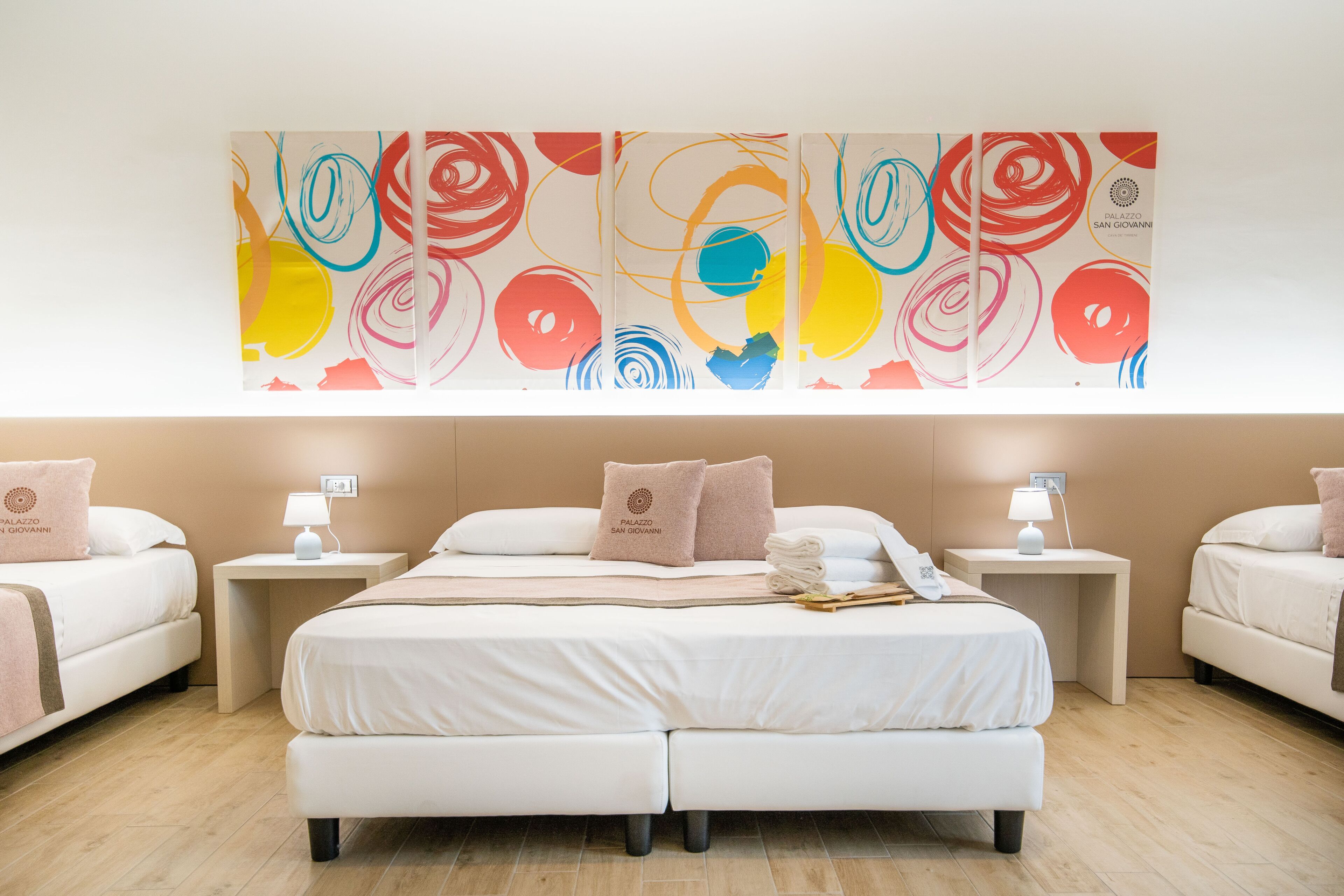 Una habitación de hotel con una cama grande, dos mesitas de noche, una obra de arte en la pared y una pequeña mesa con una lámpara.