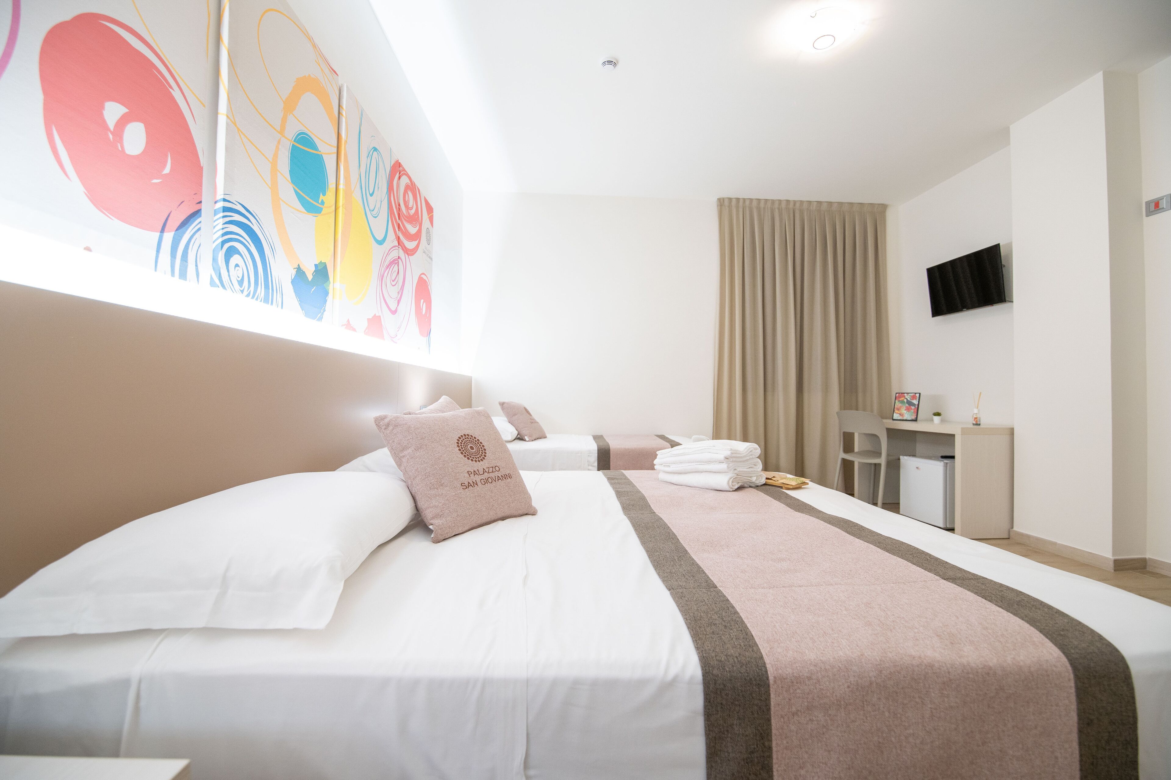 Ein Hotelzimmer mit einem großen Bett, einem Schreibtisch, einem Stuhl, einem Fernseher und einem Fenster mit Vorhängen.