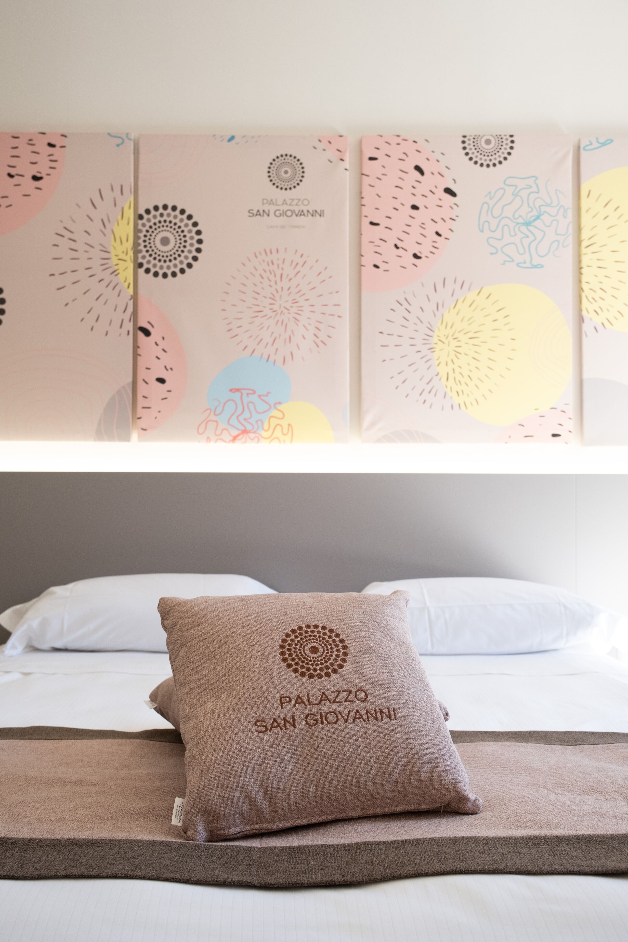 A hotel room with a bed, a pillow with the hotel name, and abstract wall art.