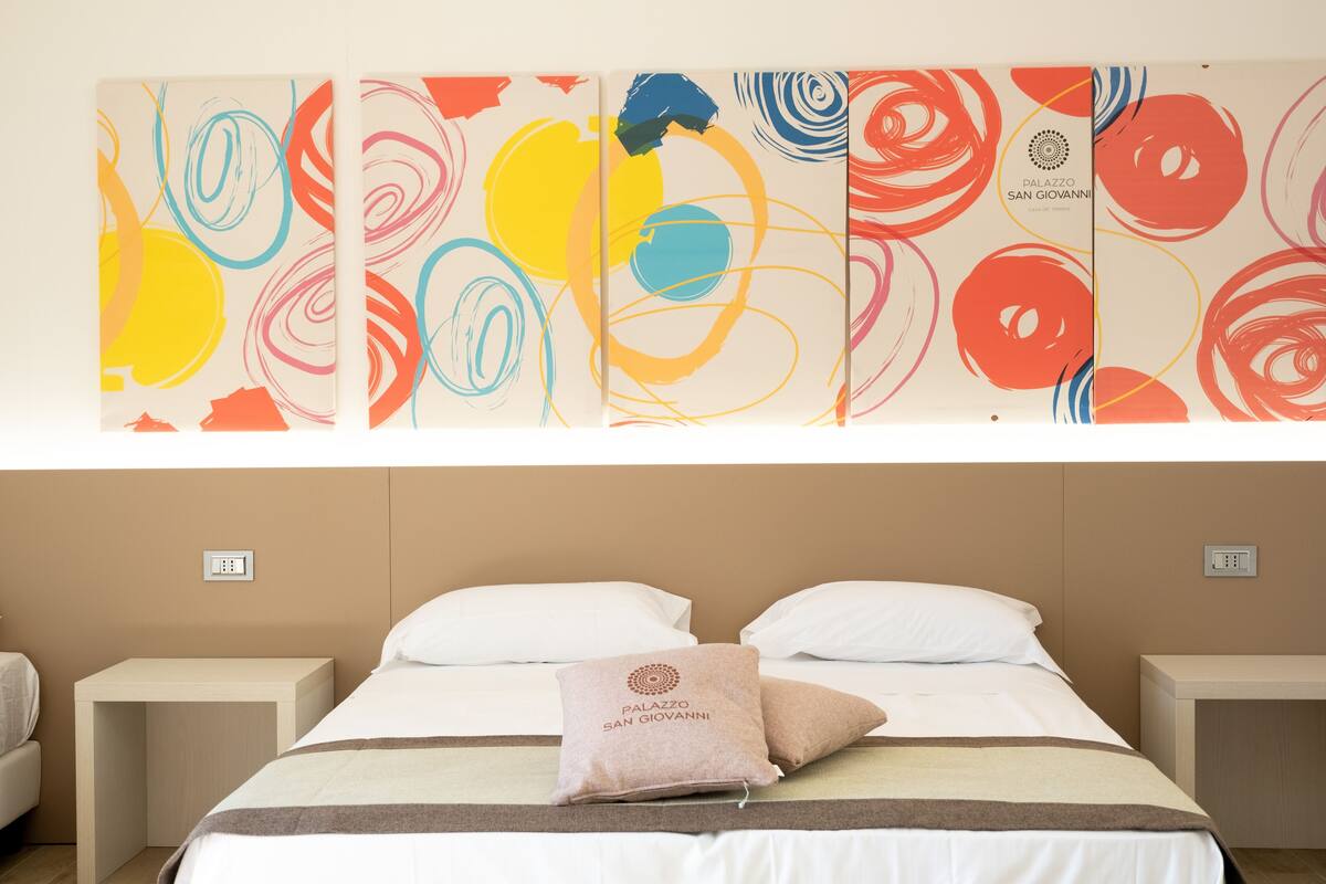 Een hotelkamer met een bed, twee nachtkastjes en een kleurrijk abstract kunstwerk erboven.