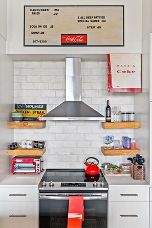 A kitchen with a menu board, a toaster, a kettle, and various kitchen items on shelves.