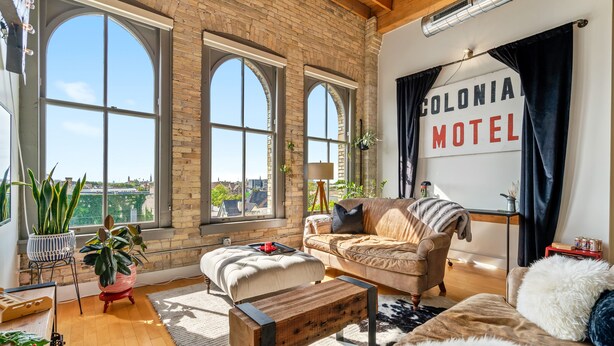 Ein geräumiges Wohnzimmer mit großen Bogenfenstern, einem gemütlichen Sofa, einer hölzernen Bank und einem Schild mit der Aufschrift 'Colonial Motel'.