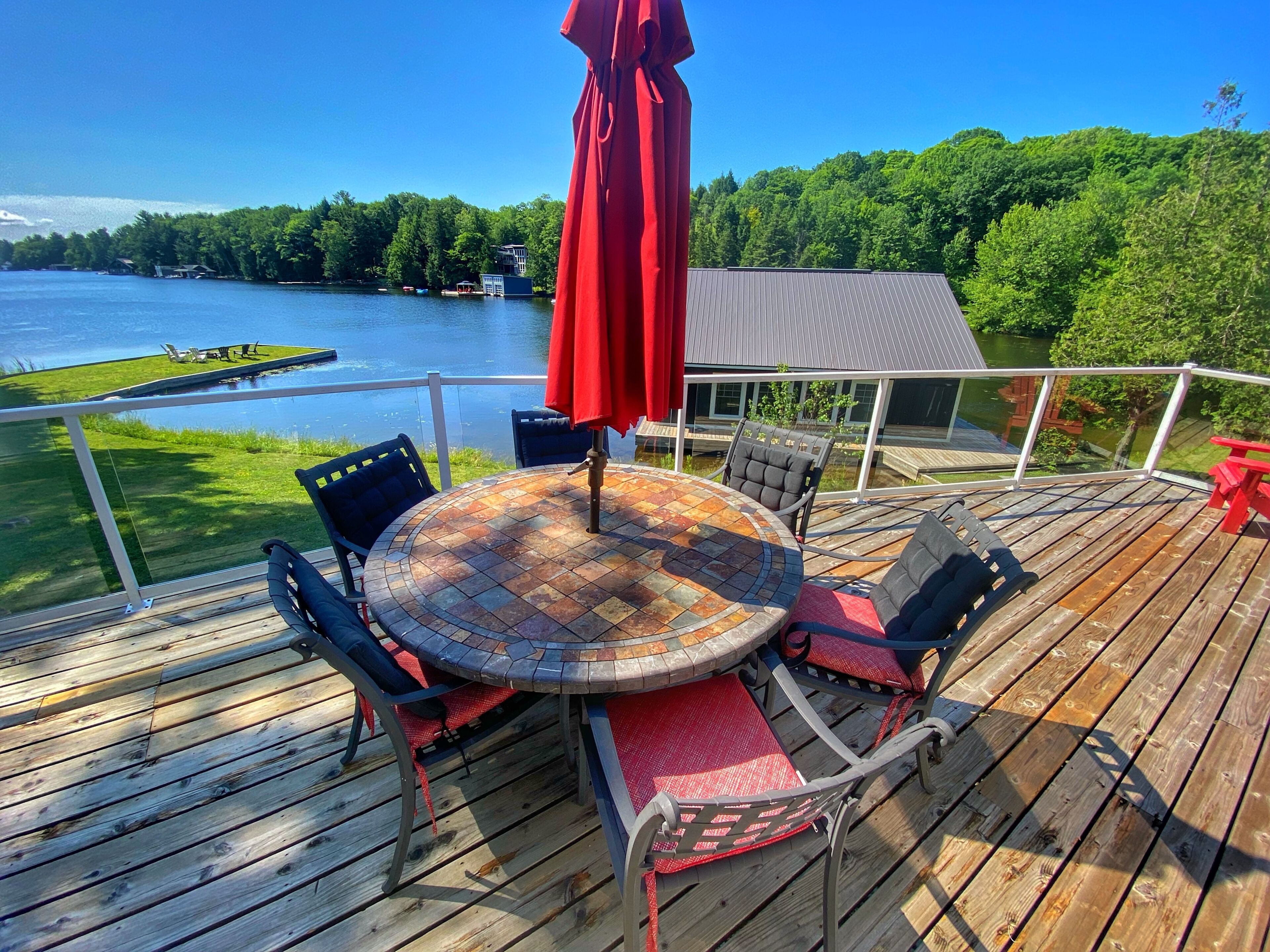 Eine Holzterrasse mit rundem Tisch und Stühlen, mit Blick auf einen See mit einem Steg und Booten.