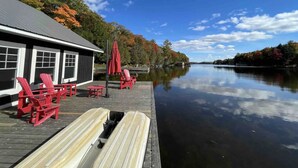 A dock with red Adirondack chairs, a wooden bench, and a building with large windows. - Stillwater Lakehouse • 20 Acre Lakefront • Sandy Beach • Dock • Firepit! (Port Carling)