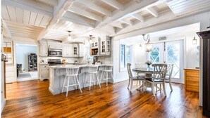 A spacious kitchen with white cabinetry, a central island with bar stools, and a dining area with a table and chairs. - Stillwater Lakehouse • 20 Acre Lakefront • Sandy Beach • Dock • Firepit! (Port Carling)