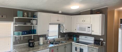 A compact kitchen with white cabinets, a microwave, stove, and a ceiling fan.