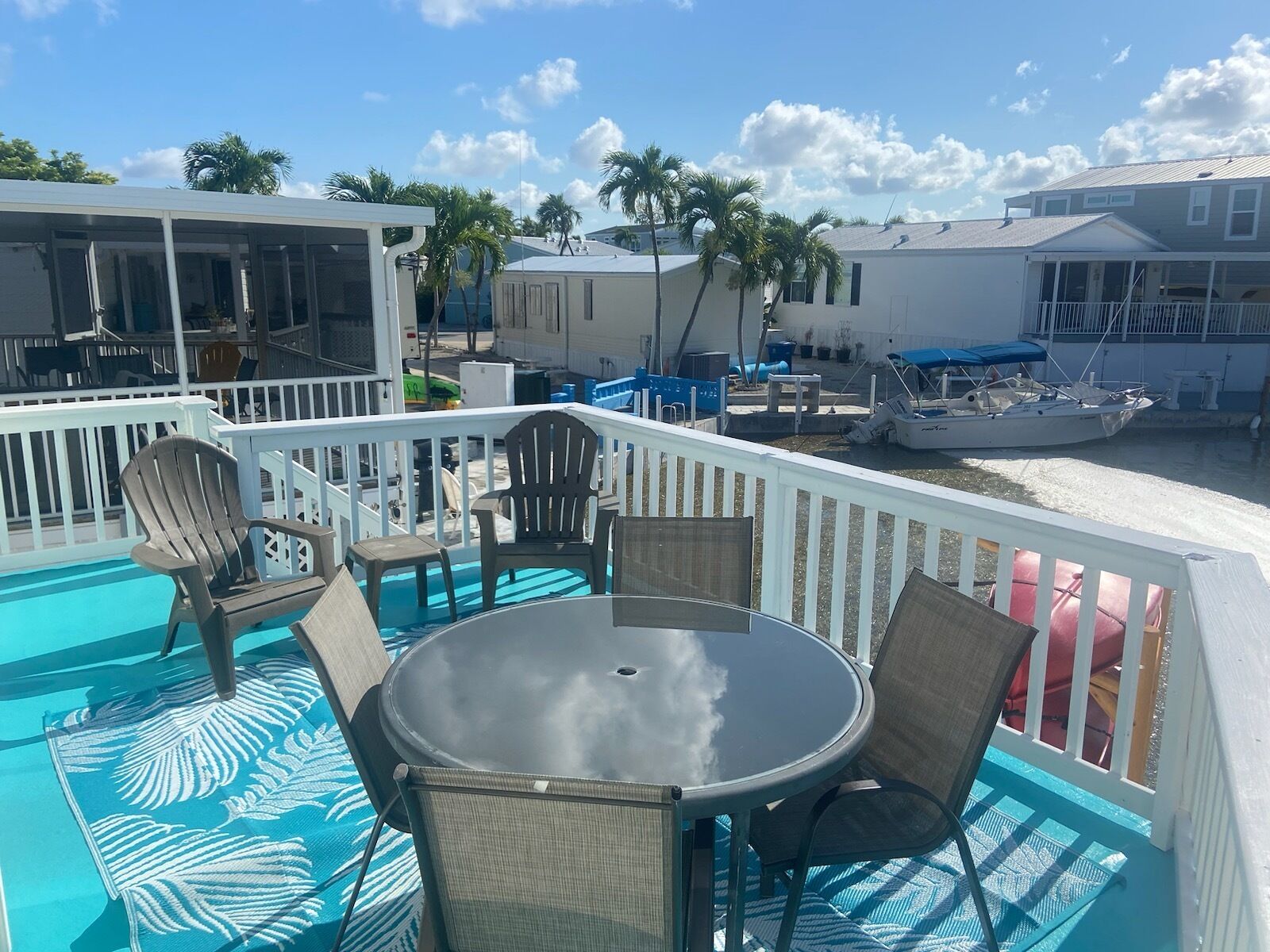 A poolside area with a table and chairs, a boat docked nearby, and a view of the ocean and other buildings.