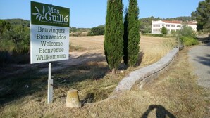 A sign welcoming visitors to Mas Guillo with a rural landscape in the background. - Mas Guilló Nursery (Sant Quintí de Mediona)