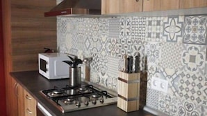 A kitchen with wooden cabinets, a gas stove, a microwave, and patterned backsplash tiles. - Mas Guilló Nursery (Sant Quintí de Mediona)