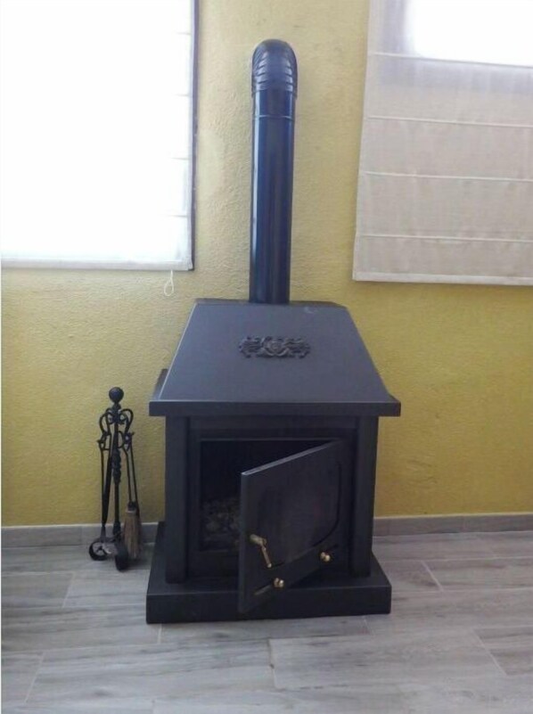 Un poêle à bois noir avec une cheminée, un élément décoratif en métal sur le dessus, et un petit support en métal avec un balai à côté.
