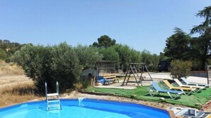 An outdoor swimming pool with a wooden deck, surrounded by greenery and a clear sky. - Mas Guilló Nursery (Sant Quintí de Mediona)