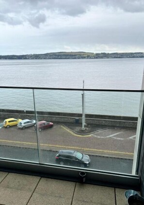 A balcony with a view of a body of water and parked cars.