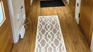 A hallway with wooden flooring, a patterned rug, and a white door with a handle. - Luxury 2 bed waterfront apartments (seaview) (Dundee)