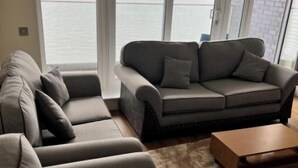 A modern living room with a sofa set, a coffee table, and a view of a body of water through large windows. - Luxury 2 bed waterfront apartments (seaview) (Dundee)