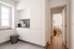 Compact kitchen area with microwave, kettle, and sink, adjacent to a cozy bedroom with a bed and nightstand.