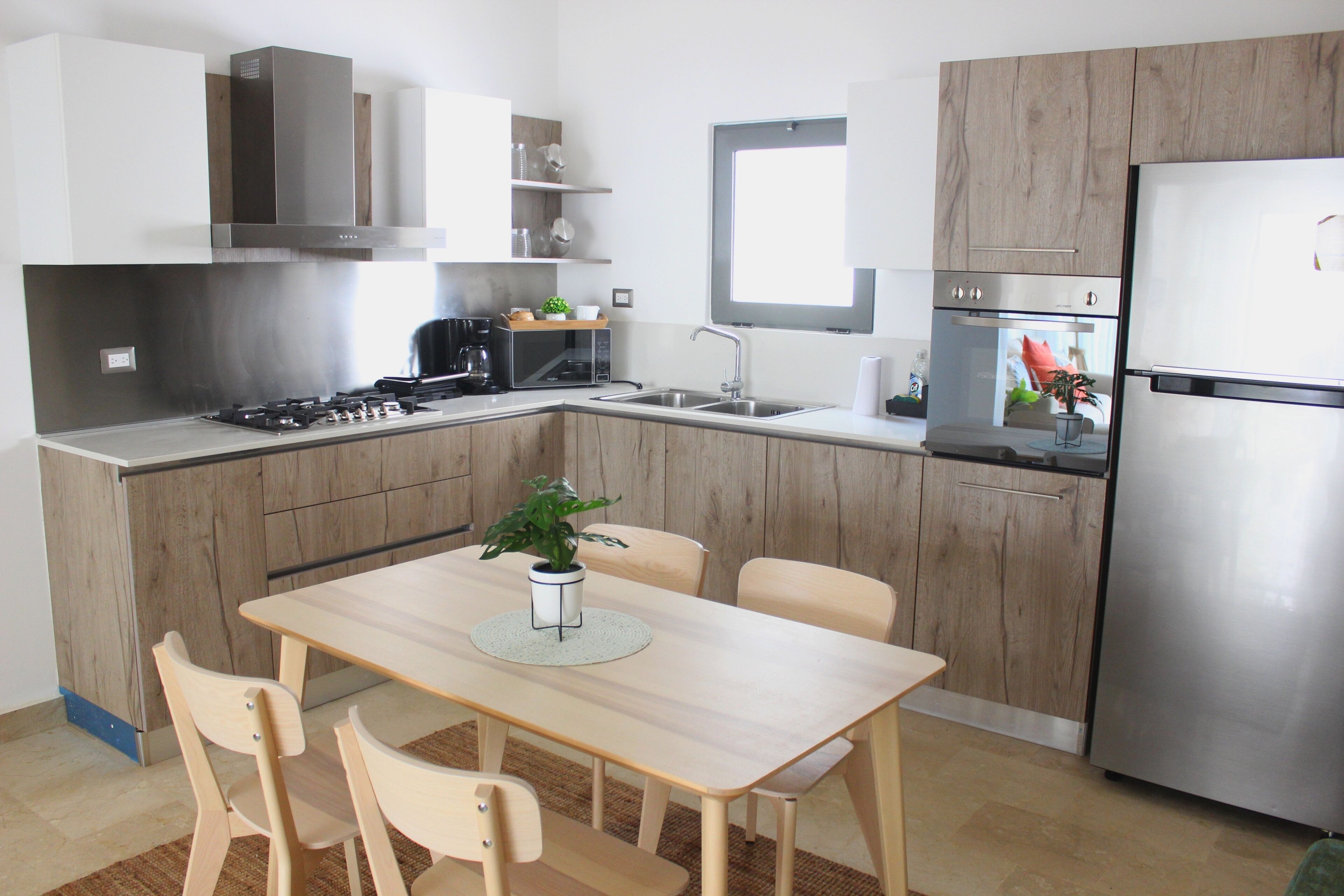 Una cocina moderna con armarios de madera, un refrigerador de acero inoxidable, un horno empotrado, un lavabo y una mesa de comedor con sillas.
