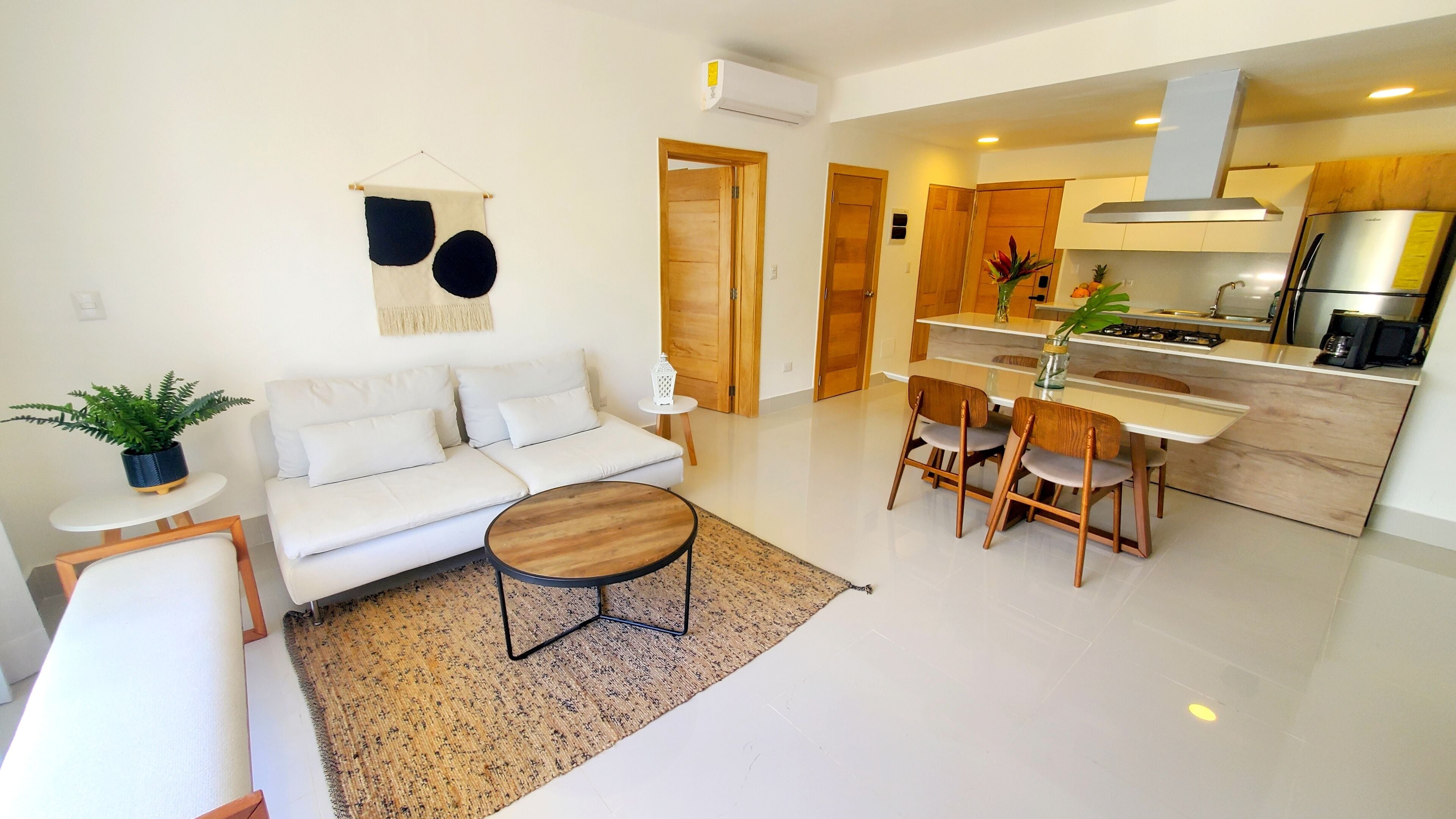 A modern living room with a white sofa, a wooden coffee table, and a dining area with wooden chairs.