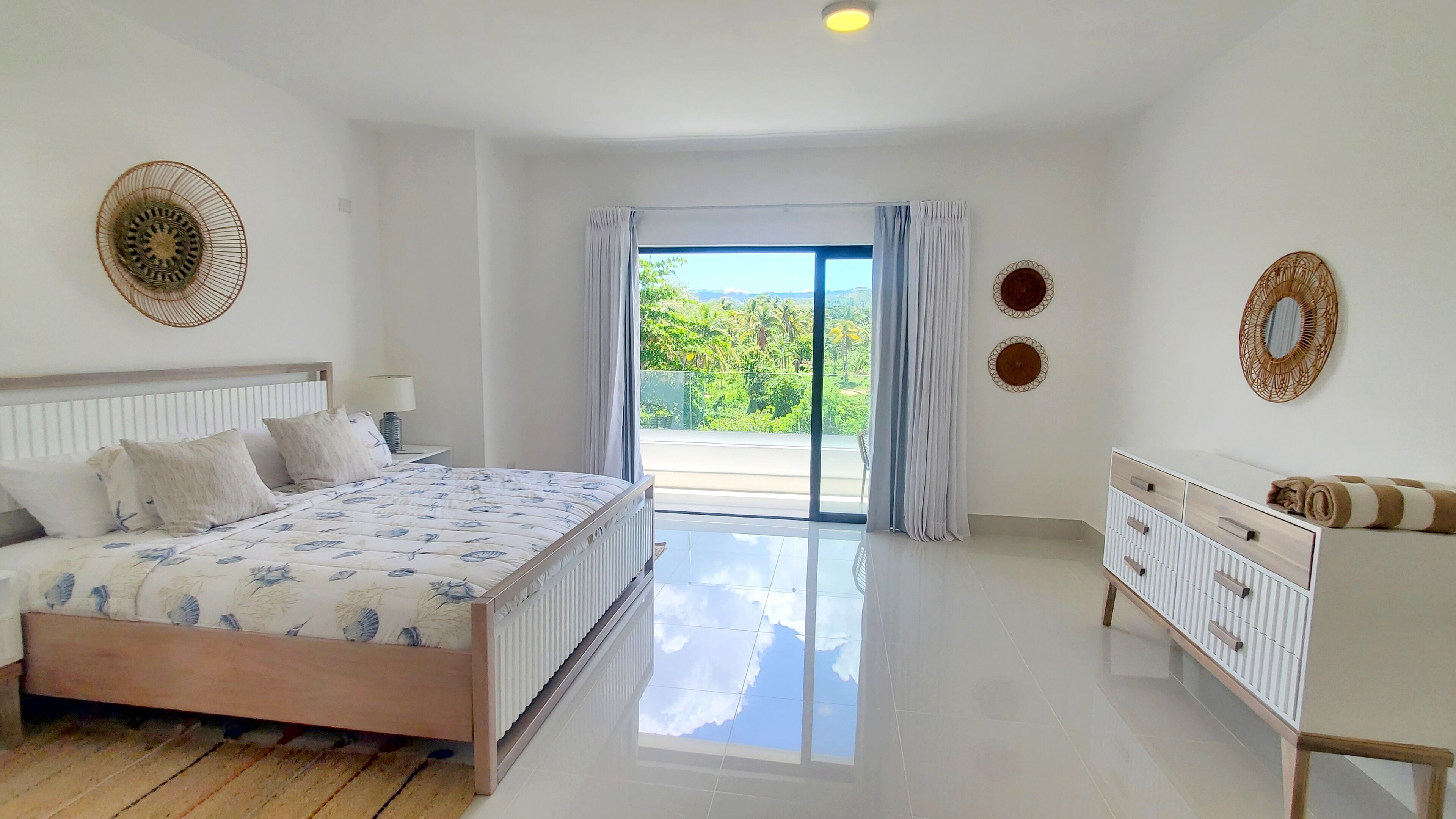 Quarto com cama, cômoda e vista para o verde lá fora.