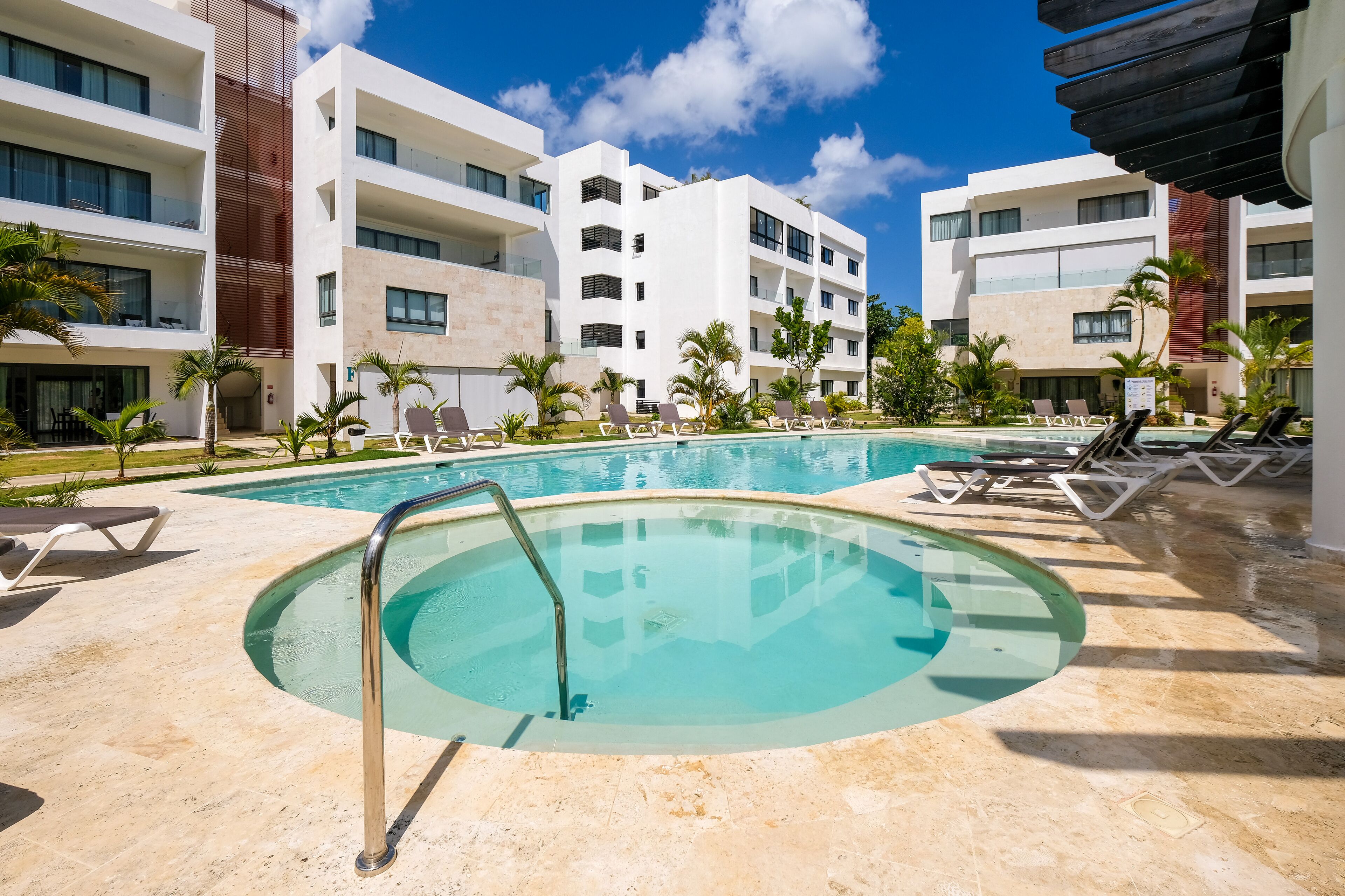 Un hotel moderno con piscina, tumbonas y palmeras.