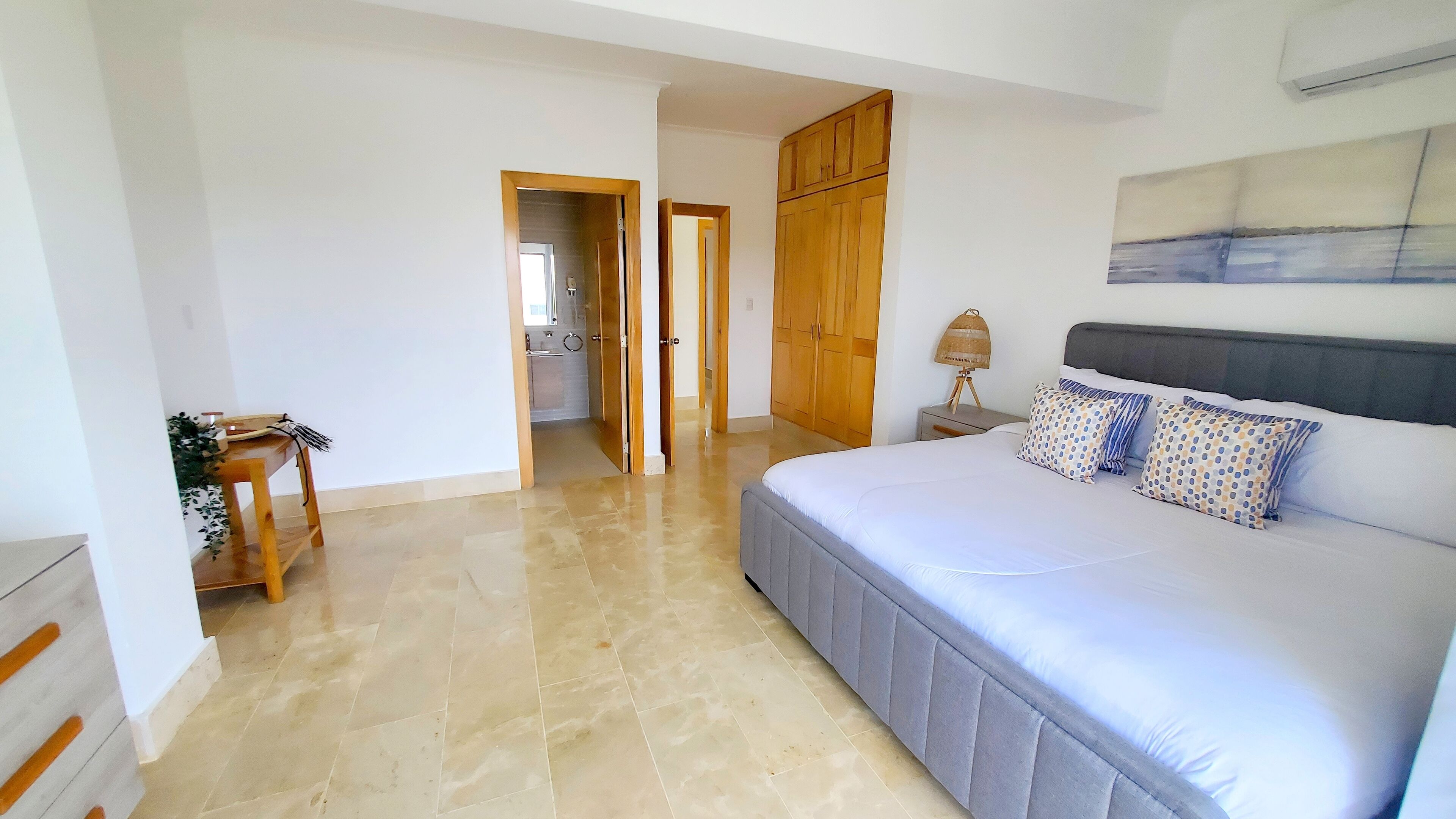A bedroom with a large bed, wooden wardrobe, and a bathroom visible through an open door.